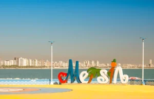 Mersin merkez sahil bandında yer alan Mersin şehir logosu, arkada masmavi Akdeniz ve şehrin modern silüeti.