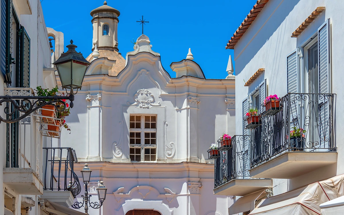 Anacapri merkezinde Santa Sofia Kilisesi ve balkonlarından çiçekler sarkan geleneksel beyaz binalar.