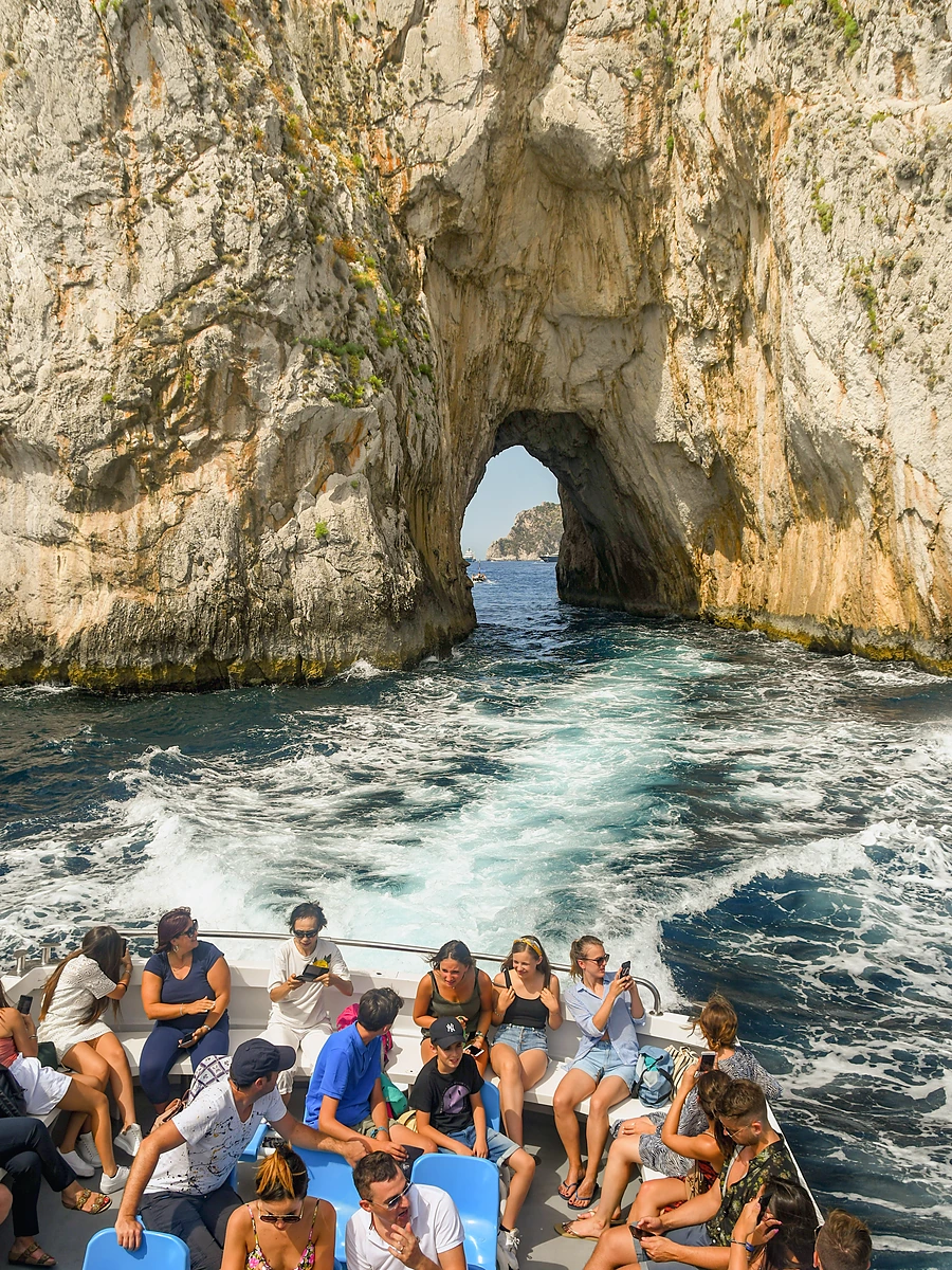 Capri Adası Faraglioni kayalıkları arasından tekneyle geçiş ve turistler.