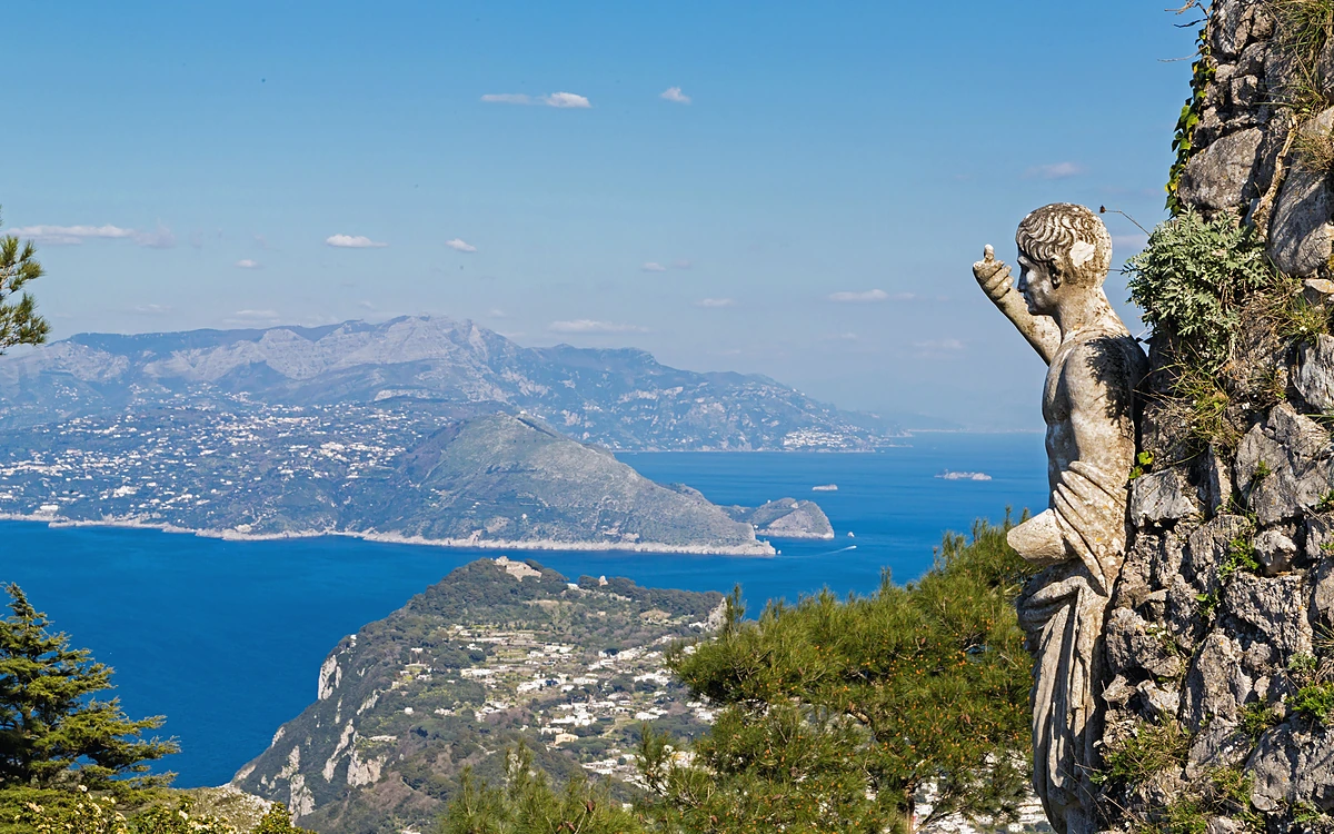 Monte Solaro zirvesindeki antik heykelin arkasında uzanan panoramik Capri ve anakara manzarası.