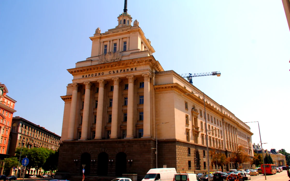 Sofya'daki anıtsal Ulusal Meclis binasının dış cephesi; sütunlu giriş, kule ve önündeki cadde trafiği.