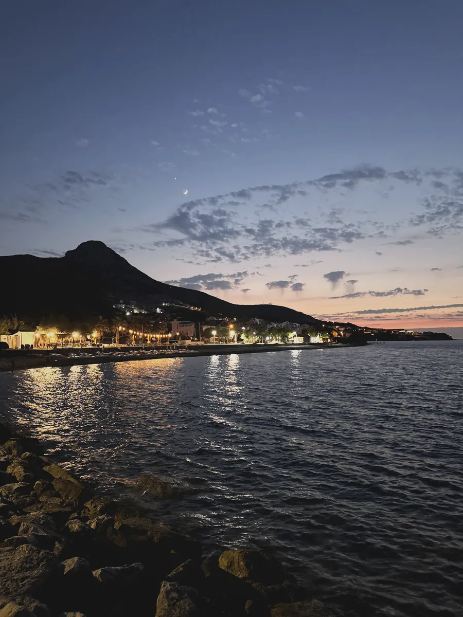 Karaburun'da alacakaranlıkta ışıkları denize yansıyan dağlık kıyı yerleşimi