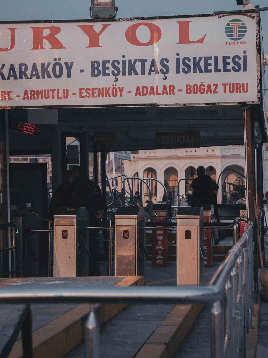 İstanbul'da bir vapur iskelesinde turnikeler ve üstte sefer bilgilerini gösteren bir tabela.